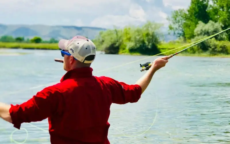 Man casting fly rod in Montana river with cigar in his mouth.