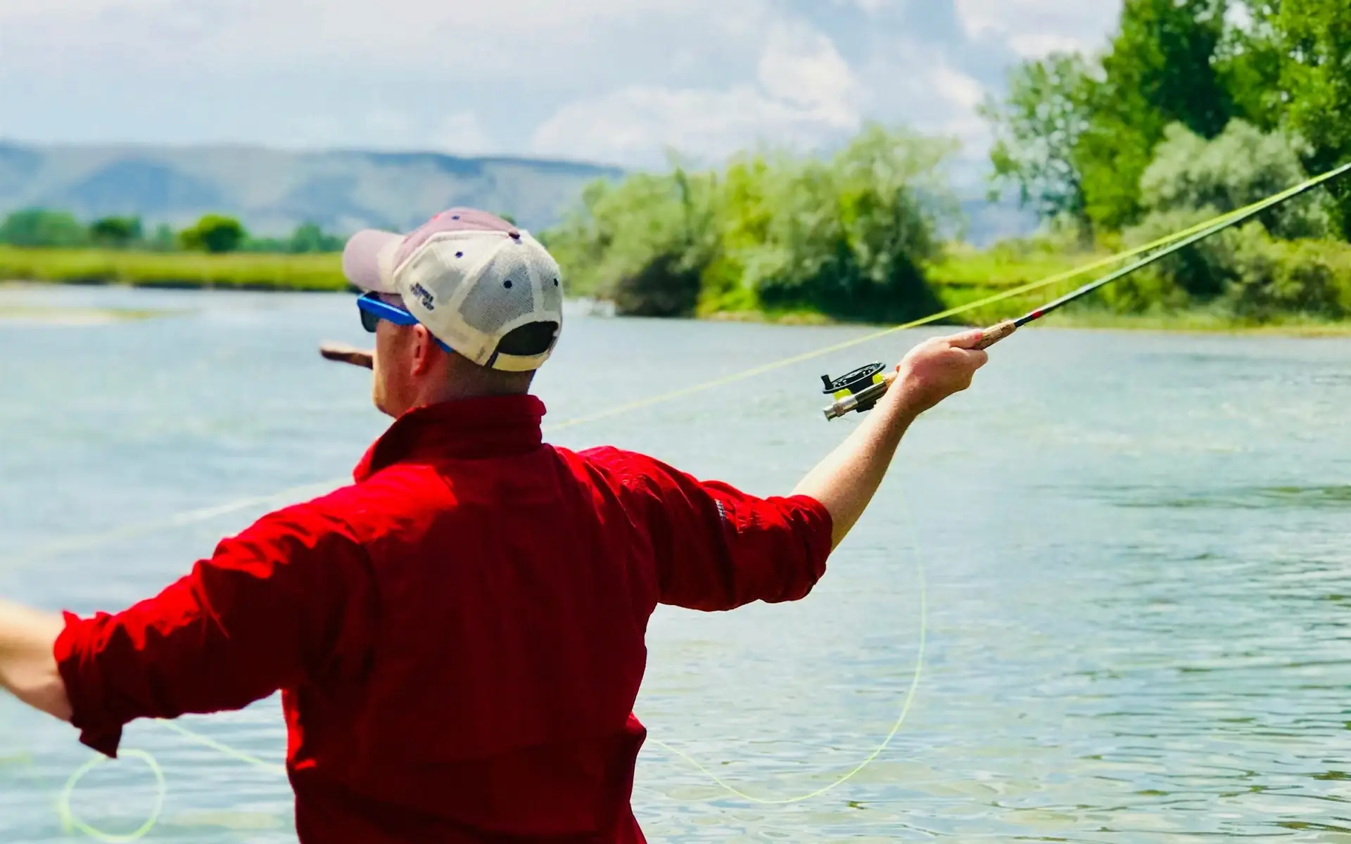 Man casting fly rod in Montana river with cigar in his mouth.