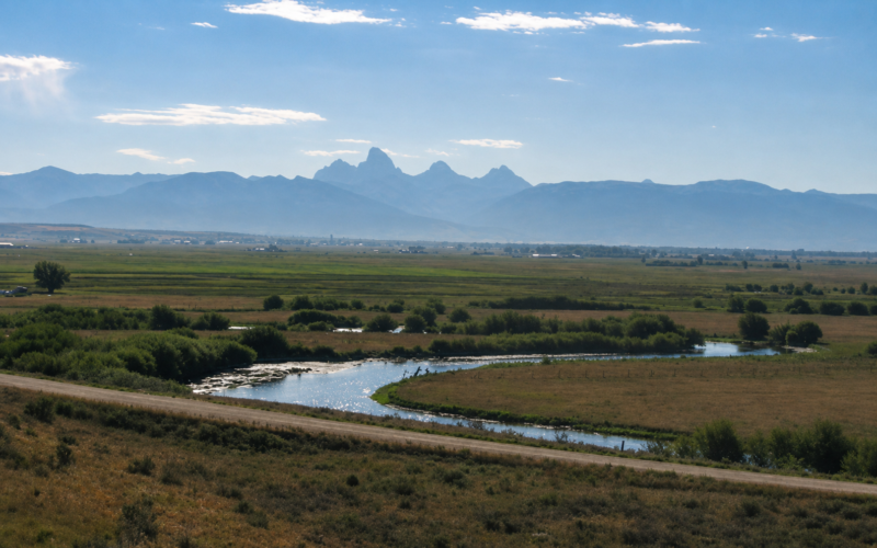 Wide valley with a winding river reflecting sunlight and distant blue mountains under a clear sky.